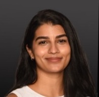 Head-and-shoulders studio portrait of a person with long dark hair wearing a light-colored sleeveless top, facing the camera against a dark gray background.