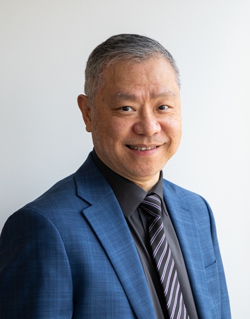 Professional headshot of a person wearing a blue suit jacket, black dress shirt, and striped tie, standing against a light gray background. The portrait is cropped from the chest up, with the subject facing slightly to the side while looking toward the camera. Soft, even lighting creates a clean and polished appearance suitable for a professional profile or organizational directory.