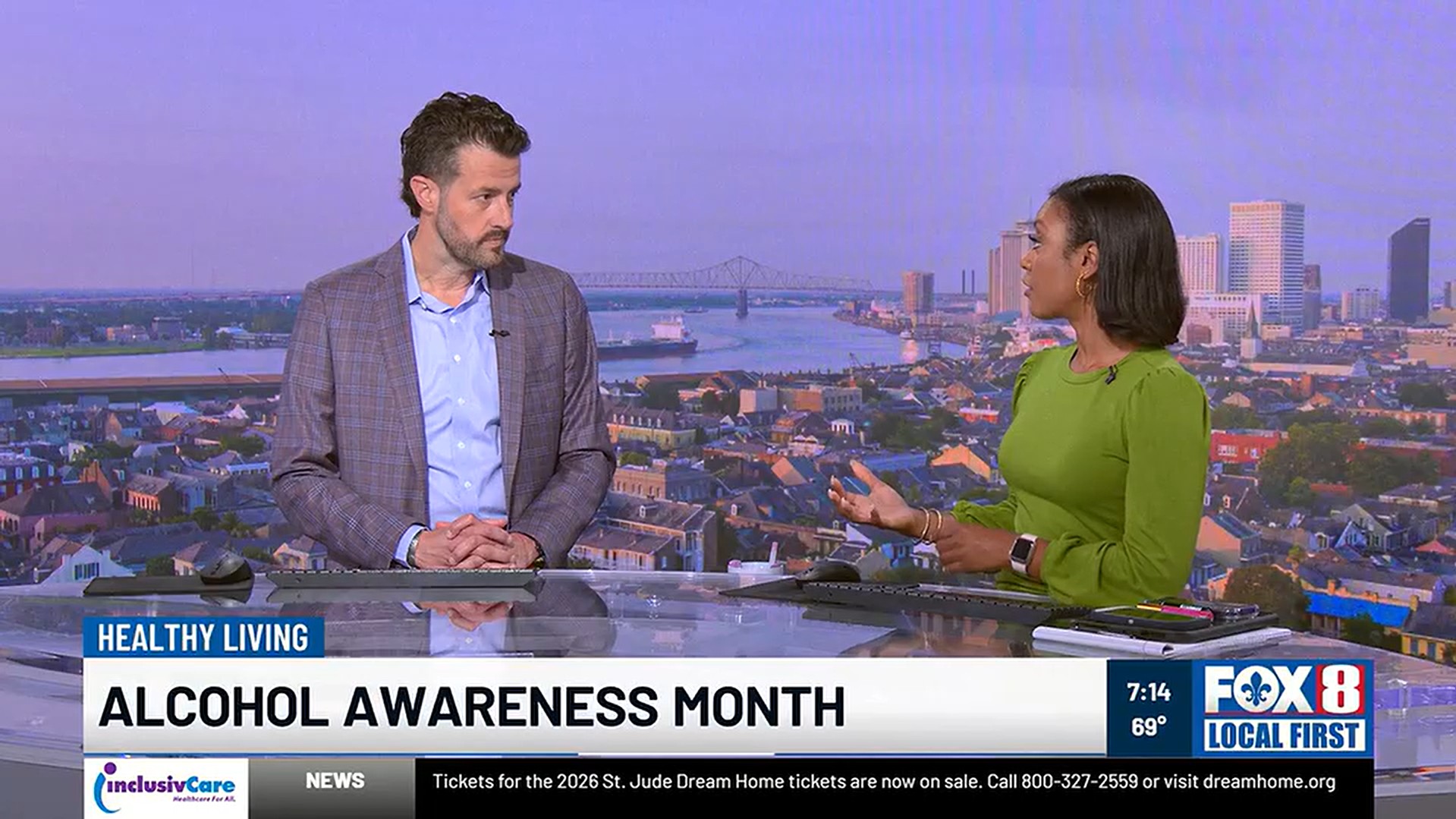  Television news studio scene showing two presenters standing behind a desk and talking, with a city skyline and river in the background. A lower-third graphic reads “HEALTHY LIVING” and “ALCOHOL AWARENESS MONTH.” The screen also shows “FOX 8 Local First,” the time “7:14,” and the temperature “69°.”