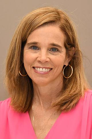Professional headshot of a person wearing a bright pink blouse and hoop earrings, posed against a neutral background.