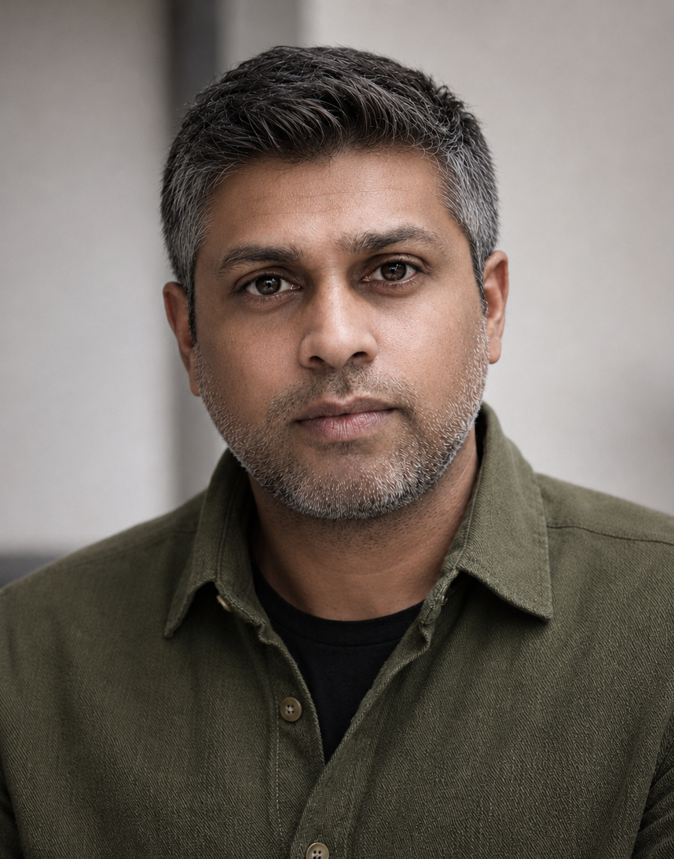 Professional headshot of a person with short salt-and-pepper hair wearing an olive-green button-up shirt, posed against a blurred indoor background.