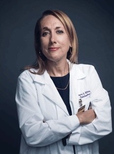 Professional headshot of a person wearing a white medical coat over a dark top, with arms crossed against a dark blue background.  Provide your feedback on BizChat