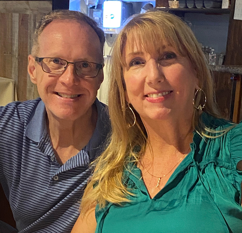Kimberly Benedict, a nurse and Merkel cell carcinoma clinical trial patient, sits beside her husband at a restaurant, reflecting hope and gratitude for cancer care and support from her family and care team.