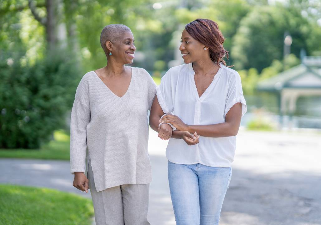 Two women walk together outdoors, smiling and talking, representing patient support, survivorship, and shared cancer care journeys.