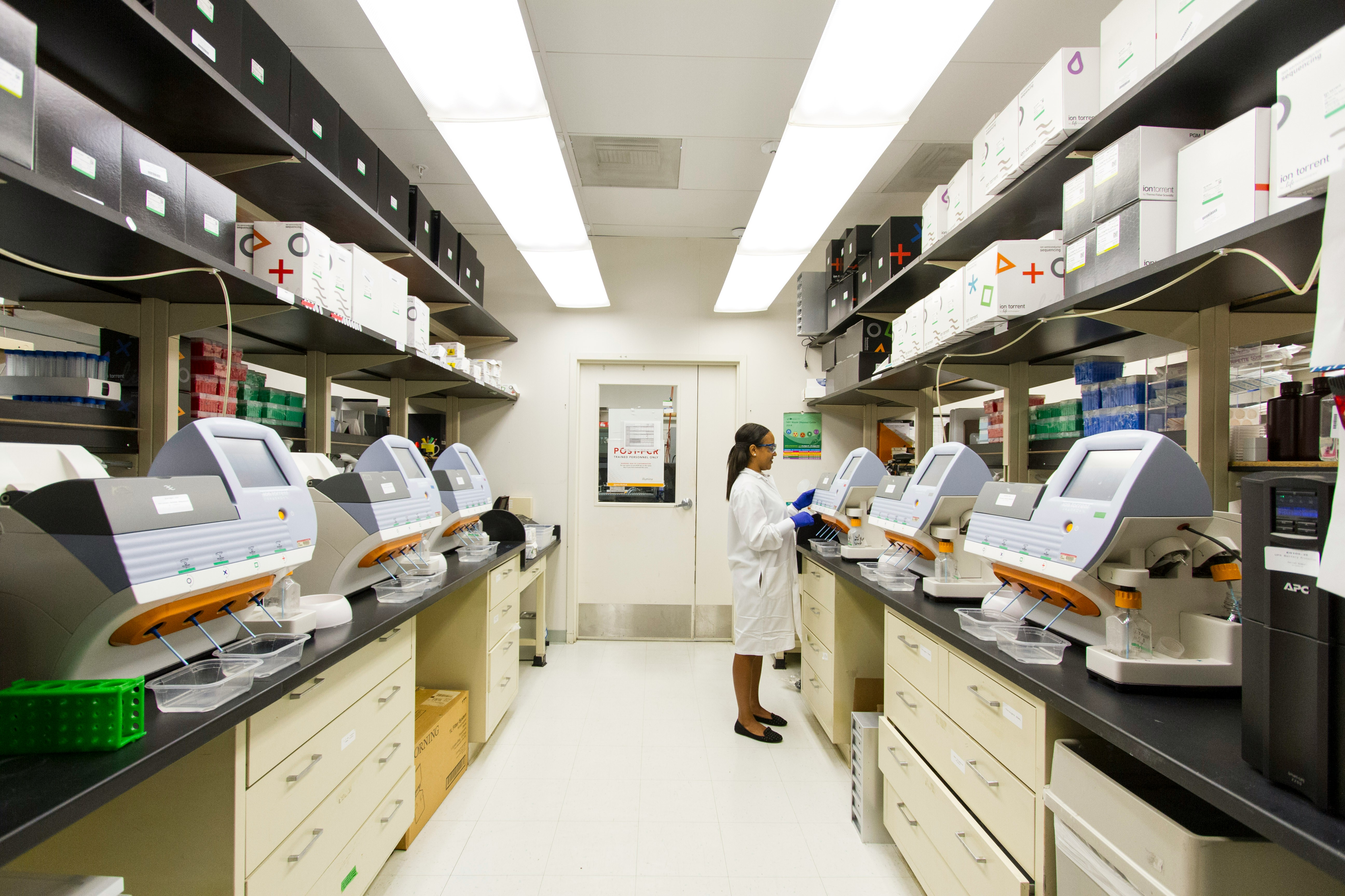 Scientist working in a modern laboratory with multiple research machines and shelves stocked with supplies