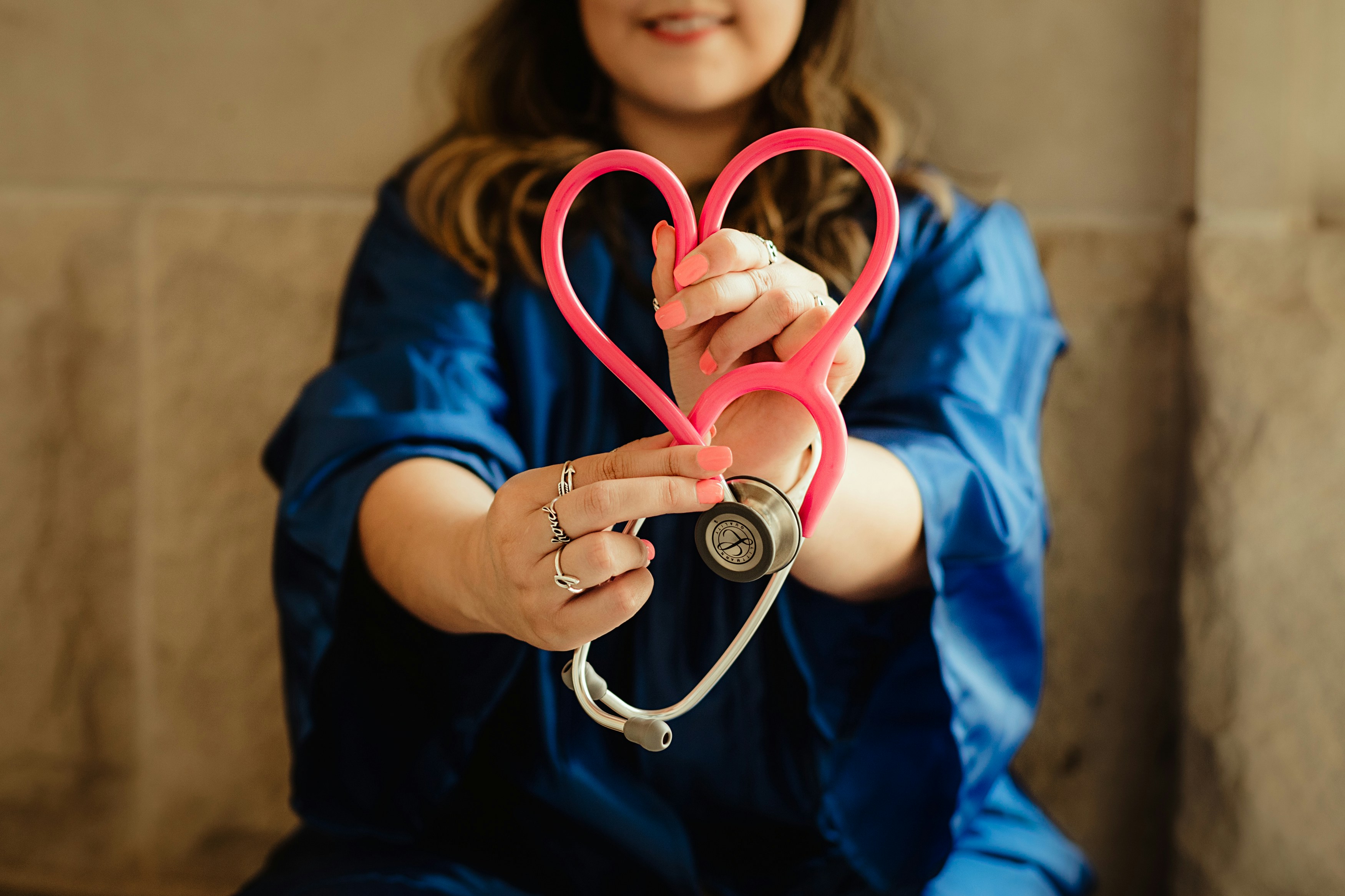 Woman in blue holding a pink stethoscope shaped like a heart, symbolizing compassion and care in healthcare.