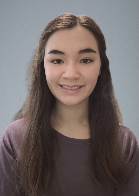 Head-and-shoulders portrait of a person with long, straight dark hair wearing a long-sleeved mauve top. The person is facing the camera against a plain light gray background. The image is closely framed around the head and upper torso and lit with soft, even lighting, similar to a school or professional portrait photograph.