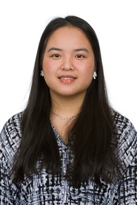 Professional head-and-shoulders portrait of a person with long, straight dark hair wearing a patterned black-and-white blouse. Small earrings and a delicate necklace are visible. The person is facing the camera against a plain light gray background. The image is framed from the chest up and lit with soft, even studio lighting, similar to a professional or academic portrait.