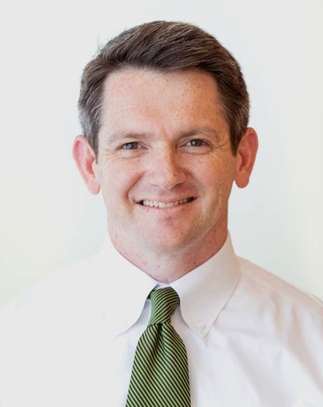 Professional head-and-shoulders portrait of a person against a plain light background. The person is facing the camera and wearing a white button-down dress shirt with a green striped necktie. The image is well lit and closely cropped, showing the upper torso and face.