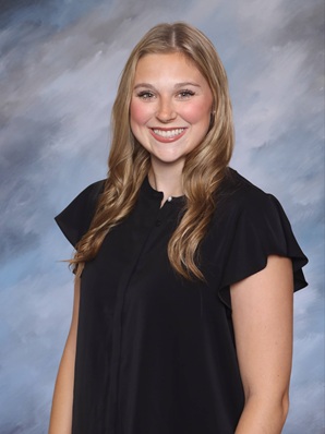Professional studio portrait of a person wearing a navy blouse against a light blue and gray textured background.