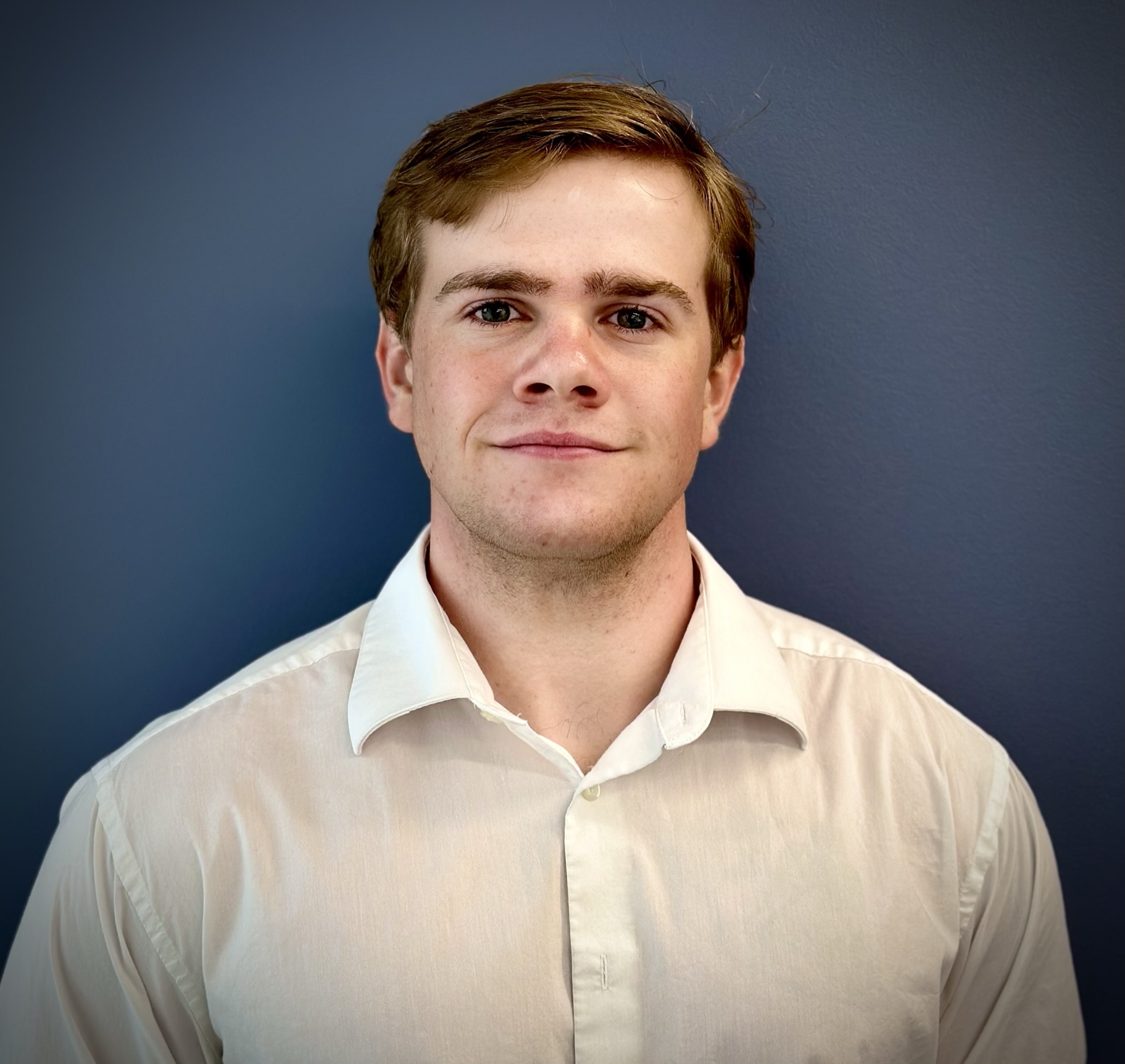 Professional headshot of a person wearing a white button-down shirt against a dark blue background.