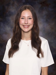 Professional studio portrait of a person wearing a white blouse against a mottled blue-gray background.