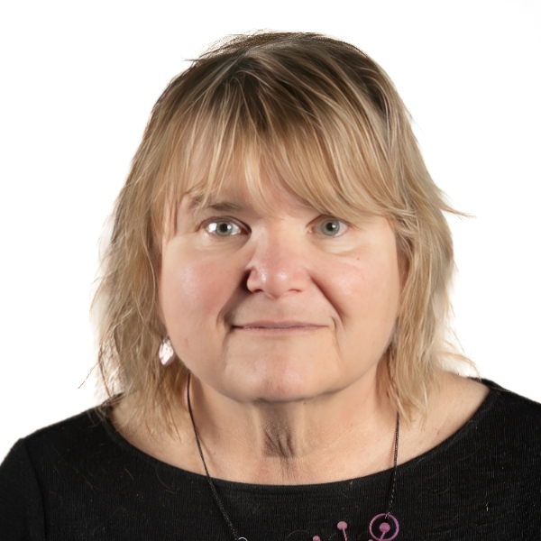Professional headshot of a person with shoulder-length light hair wearing a black top against a light gray background.